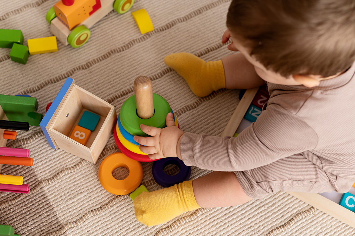 Bambino che gioca con giochi montessori in legno seduto per terra su un tappeto beige