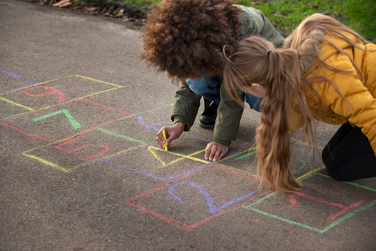 Bambini che disegnano con i gessetti colorati il gioco della campana per terra