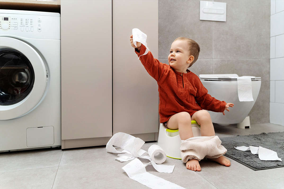 Bambino che impara ad usare il vasino e che gioca con la carta igienica