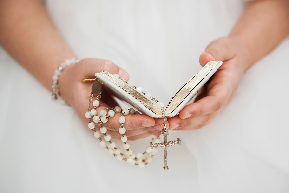 bambina che tiene in mano un rosario e una bibbia mentre celebra la prima comunione